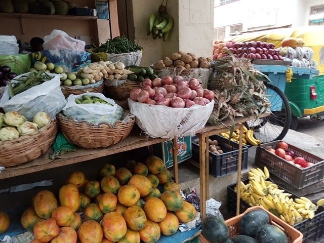 A market stall stacked with mangoes, apples, bananas, gourds and leaf vegetables.